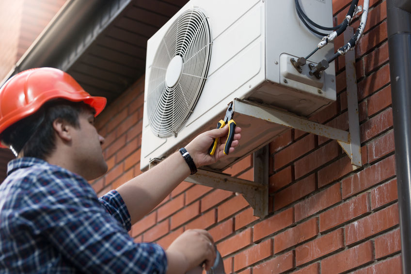 Portrait of technician in hardhat connecting outdoor air conditioning unit